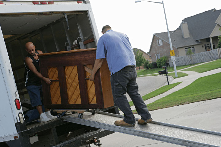 Two professional movers from Movers Plus unloading a piano from a moving truck down a ramp in a Dallas suburb, showcasing specialized moving expertise.