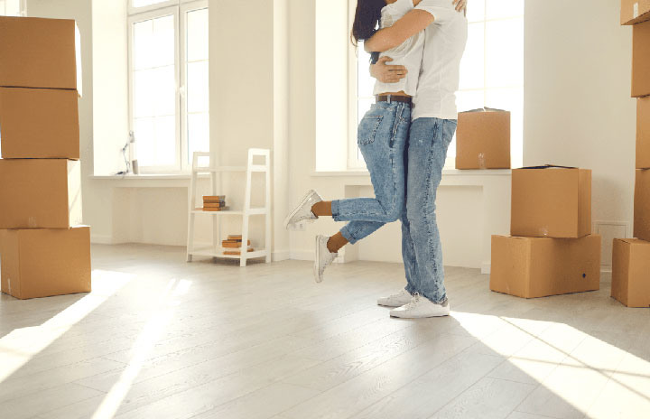 Happy couple embracing in an empty apartment surrounded by moving boxes, celebrating their new beginning with Movers Plus's services in Frisco.